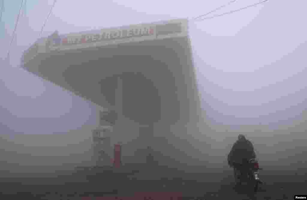 A motorcyclist arrives at a fuel station shrouded in fog on a winter morning on the outskirts of Lahore, Pakistan.