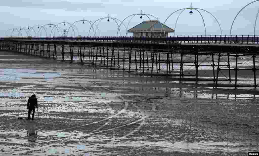 A man uses a metal detector on the beach in front of Southport Pier in Southport, Feb. 20, 2024. Britain’s second longest pier has been closed for over a year for safety and structural reasons with the local council unable to fund the estimated £13 million ($16 million) repair bill.