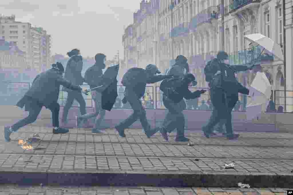 Protesters shield with umbrellas as they scuffle with riot police during rally in Nantes, western France. French unions are holding their first mass demonstrations since President Emmanuel Macron enflamed public anger by forcing a higher retirement age through parliament without a vote.