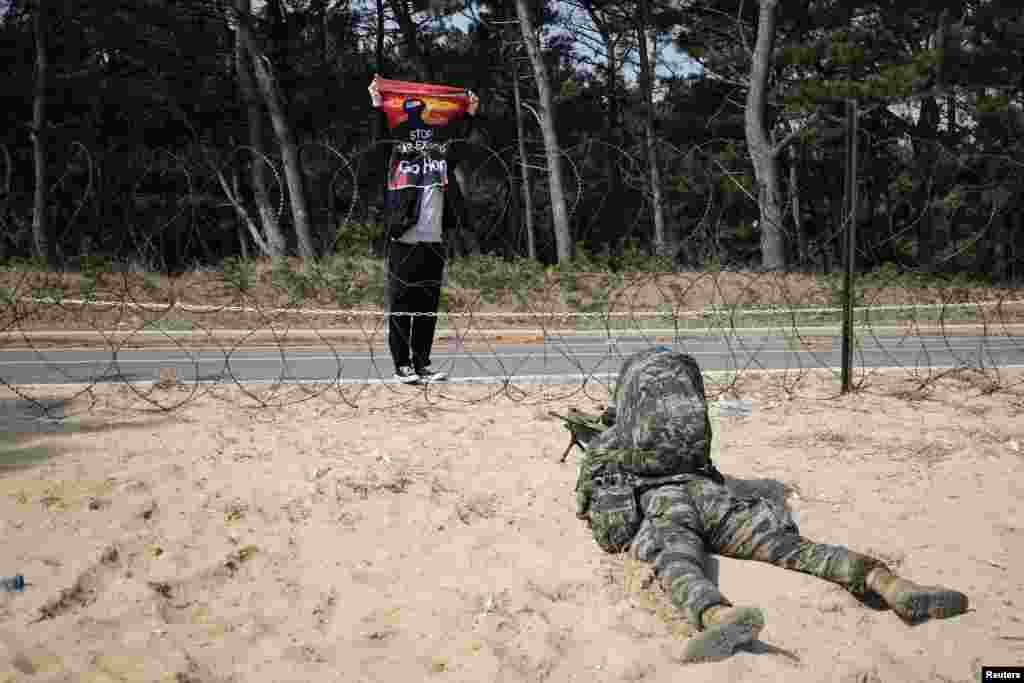 An anti-war activist holds up a sign "Stop war exercise, Go home" in front of a South Korean marine taking a position during a U.S. and South Korea marine corps combined amphibious landing drill, in Pohang.