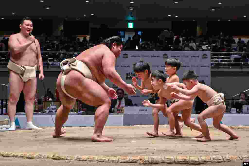 Retired Mongolian-born "yokozuna" wrestler Hakuho (far L) watches as participants (R) try to push out Japanese wrestler Hakuoho (C) during a sumo class for youngsters at the Kokugikan arena in the Ryogoku area of Tokyo.
