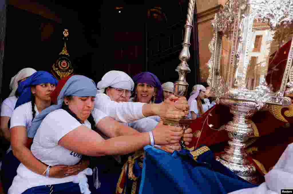 Women 'costaleras' acting as 'penitents' belonging to Cristo Resucitado y Nuestra Senora de Loreto brotherhood hold a structure in a ramp while others carry a statue of the Virgin Mary on a structure traditionally known as 'paso', as they leave a church during an Easter Sunday procession, the last day of Holy Week, in Ronda, Spain. 