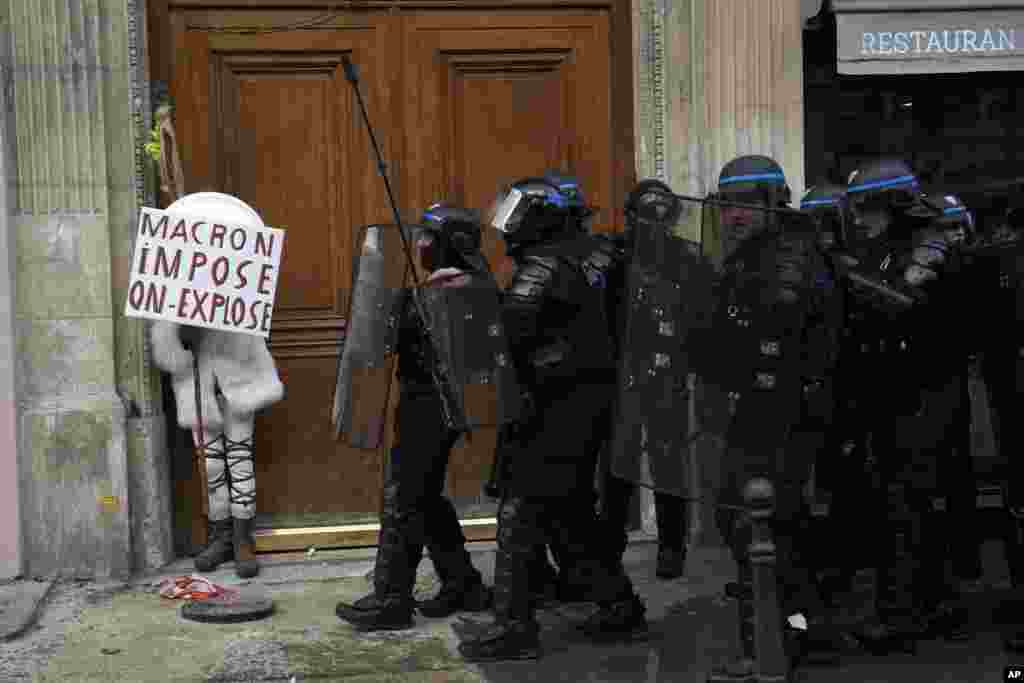 A protester hides behind a poster reading "Macron impose, we explode" during a demonstration against French President Emmanuel Macron's unpopular plan to raise the retirement age, in Paris, France.