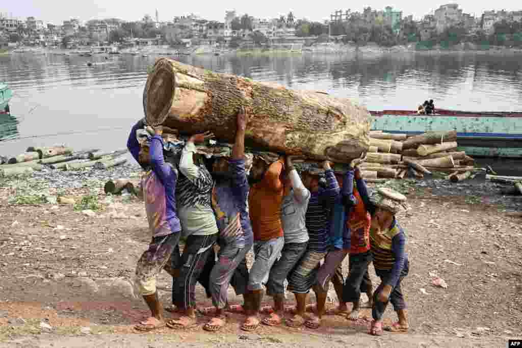 Laborers carry a log of wood from a cargo boat near the Buriganga river in Dhaka, Bangladesh.