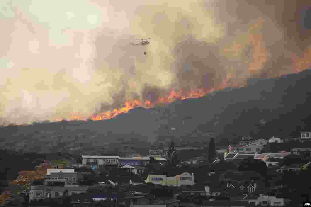 A Fire and Rescue helicopter water bombs a line of wildfire above the residential neighborhood of Glencairn, near Simon's Town, South Africa.