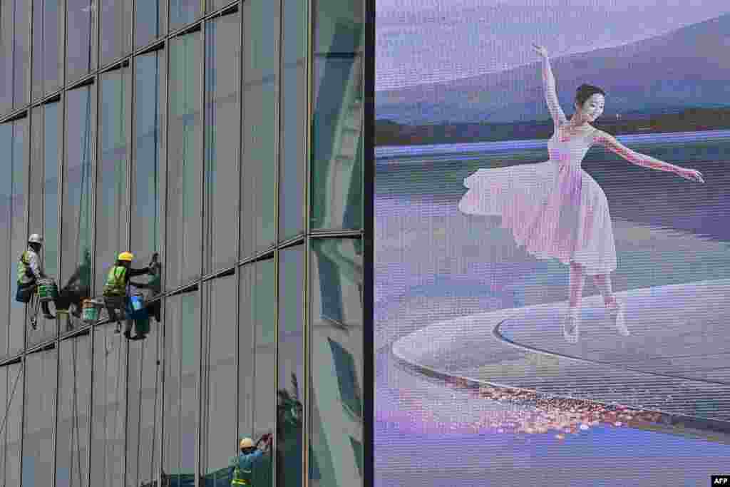 Workers clean the glass windows next to an electronic billboard on a high-rise building in Hanoi, Vietnam.