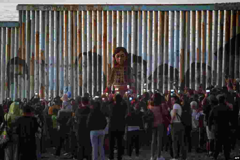 Little Amal, a 12-foot-tall puppet representing a 10-year-old Syrian refugee child, stands at the U.S.-Mexico border wall in Playas de Tijuana, Baja California, Mexico. Little Amal is visiting Tijuana within the framework of a journey across Mexico to raise awareness of the plight of refugees and migrants across the globe.