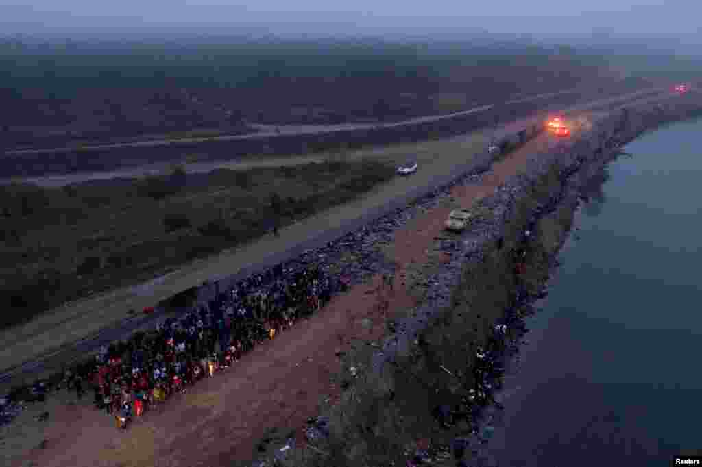Migrants, primarily from Venezuela and Honduras, are detained while others walk along the riverbank after wading across the Rio Grande River into Eagle Pass, Texas, Dec. 23, 2023.