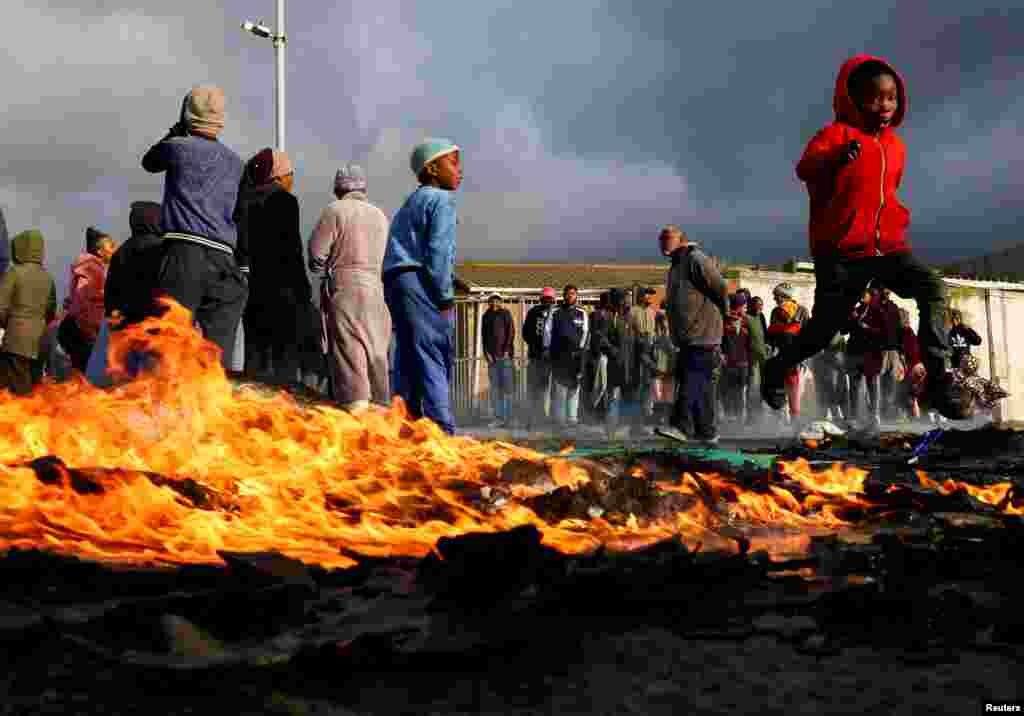 A boy runs past a burning barricade where residents from Overcome Heights, an informal settlement on the Cape Flats, protest over housing in Cape Town, South Africa.