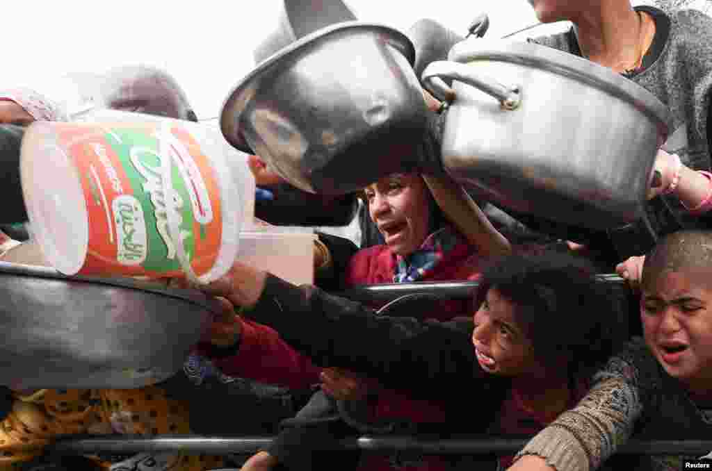 Palestinian children wait to receive food cooked by a charity kitchen amid shortages of food supplies in Rafah in the southern Gaza Strip