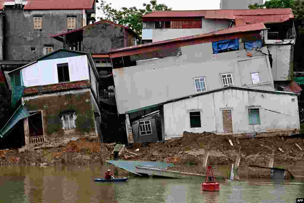 A woman on a boat looks at damaged houses on the banks of Cau River in Vietnam's Bac Ninh province.