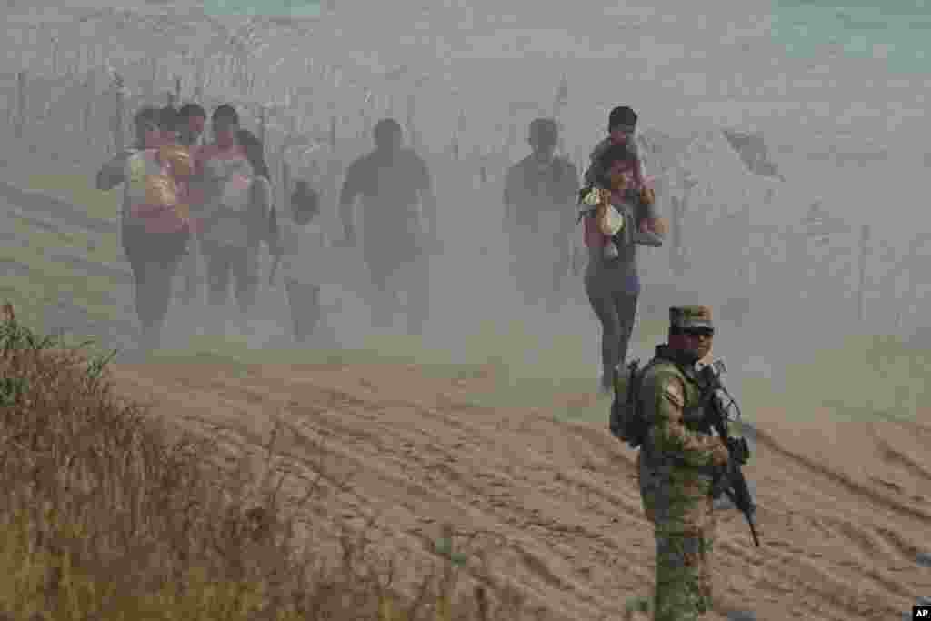 A Texas guardsman watches as migrants who crossed the Rio Grande River from Mexico to the U.S. walk along concertina wire, in Eagle Pass, Texas, July 31, 2023.