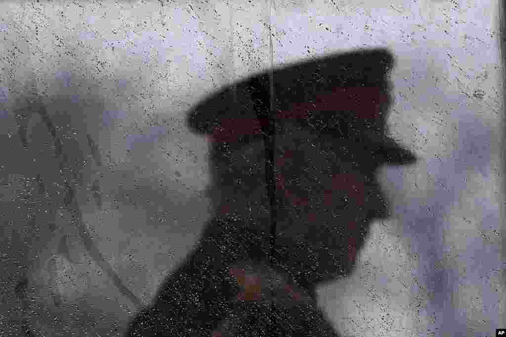 Britain's King Charles III is silhouetted behind glass covered in raindrops as he inspects the 200th Royal Military Academy Sandhurst's Sovereign's Parade in Camberley, England.