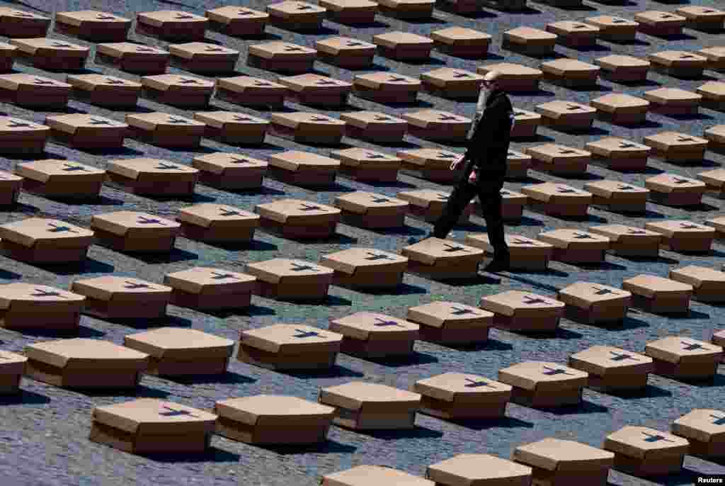A person walks past some 1040 cardboard coffins, symbolizing the number of victims who lost their lives in a workplace last year, are placed in Piazza del Popolo in Rome, Italy, during the campaign 'Zero dead at work' organized by the Italian Labor Union.
