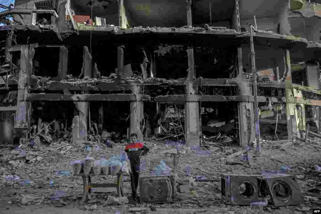A Palestinian vendor waits for customers in front of a building destroyed by Israeli bombardment in Gaza City.