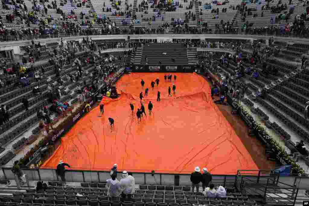 Stewards push water off the rain cover as rain delays the start of the men's final tennis match between Daniil Medvedev of Russia and Denmark's Holger Rune at the Italian Open tennis tournament in Rome, Italy.