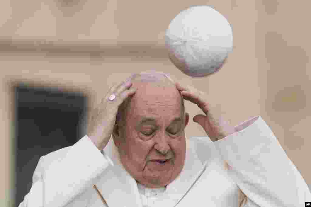 Pope Francis tries to catch his cap as wind blew it away while arriving for his weekly general audience in the St. Peter's Square at the Vatican.