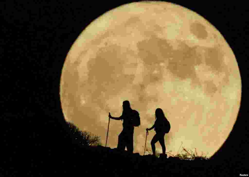 Women walk up a mountain with the full moon known as the &quot;Sturgeon Moon&quot; looms in the background, in Arguineguin, on the island of Gran Canaria, Spain, Aug. 1, 2023. 