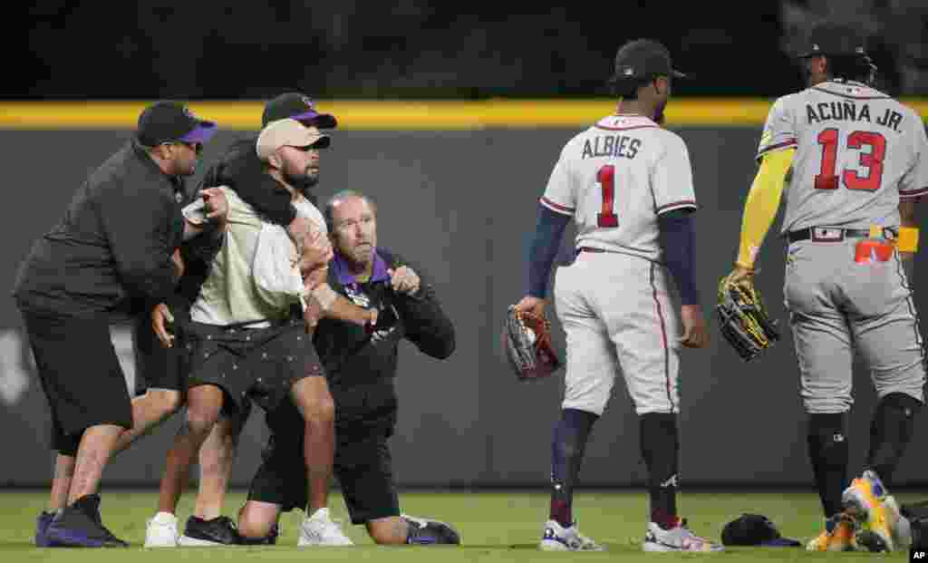 Field guards hold onto a fan as he tries to reach Atlanta Braves right fielder Ronald Acuna Jr., right, while second baseman Ozzie Albies (1) looks on in the seventh inning of a baseball game against the Colorado Rockies, in Denver, Coloardo, Aug. 28, 2023.