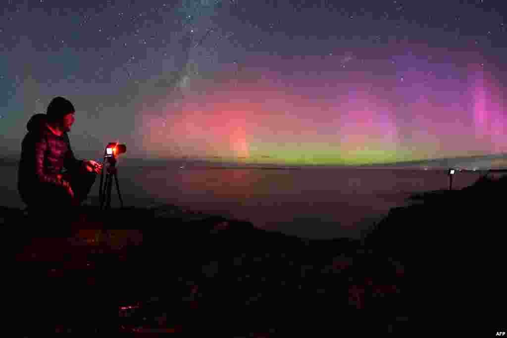 A photographer takes pictures of the Aurora Australis, also known as the Southern Lights, as it glows on the horizon over waters of Lake Ellesmere on the outskirts of Christchurch, New Zealand.