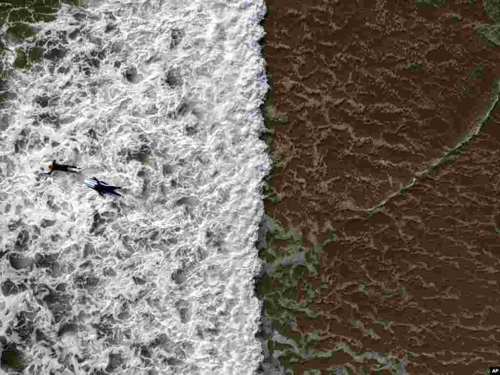 In this photo taken with a drone, two surfers wade through water in Huntington Beach, California, April 17, 2023.