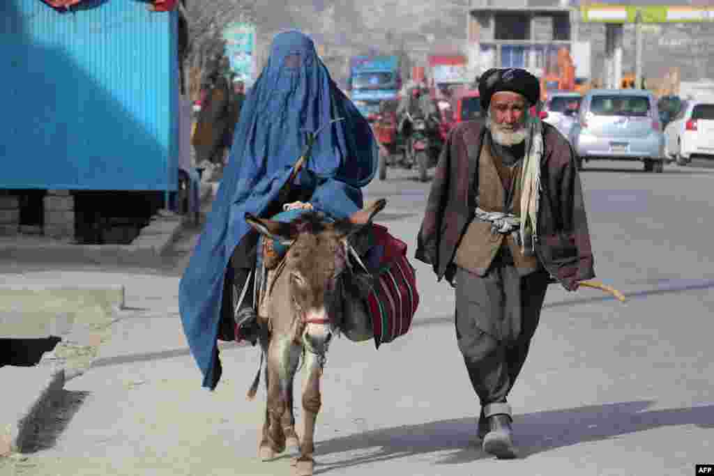 A man walks beside a burqa-clad woman riding a donkey along a street in Fayzaba, Afghanistan.