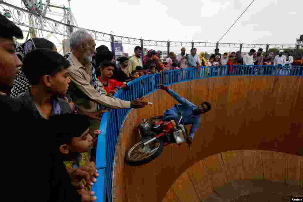 A performer extends his hand to grasp money from the audience, while riding a motorbike with one leg up on the walls of the "Well of Death", at a fair in Karachi, Pakistan.