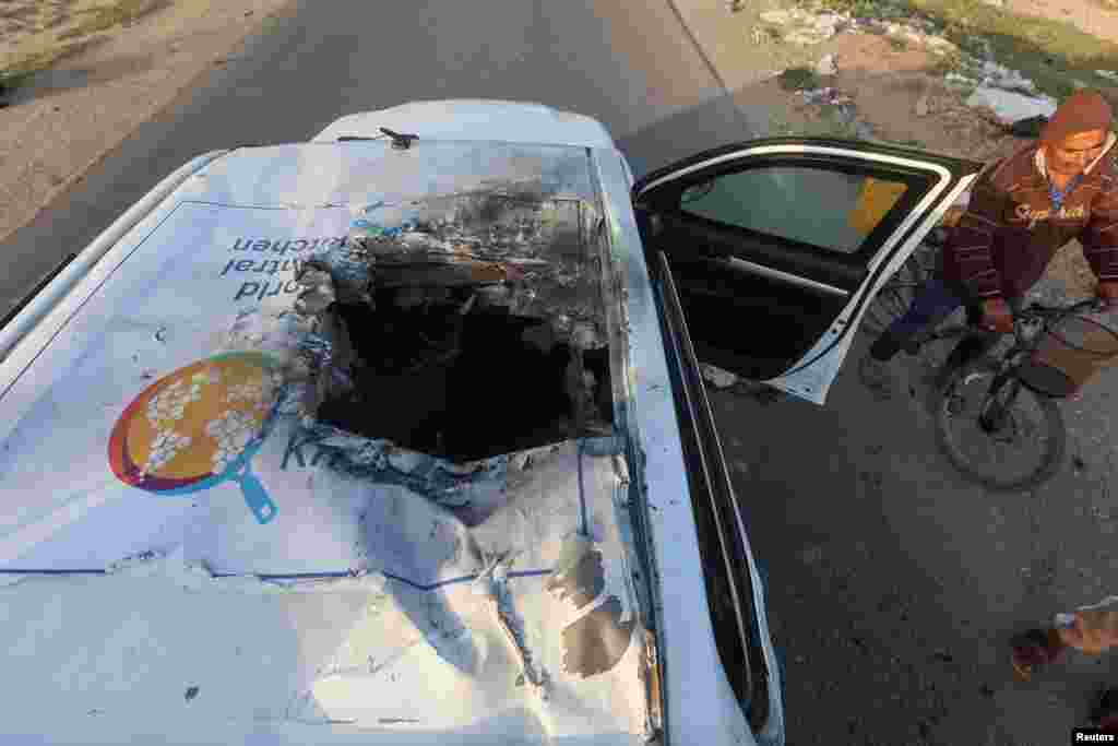 A Palestinian man rides a bicycle past a damaged vehicle where employees from the World Central Kitchen were killed in an Israeli airstrike, according to the NGO, in Deir al-Balah, Gaza Strip.