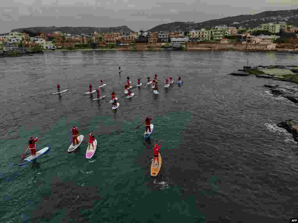People dressed in Santa Claus outfits riding on standup paddles in the Mediterranean Sea, in Lebanon's northern coastal city of Batroun, Lebanon.