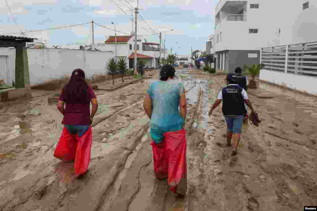 Women use bags to cover their feet and legs to walk on a street covered in mud following Cyclone Yaku in Punta Hermosa, Peru, March 15, 2023.