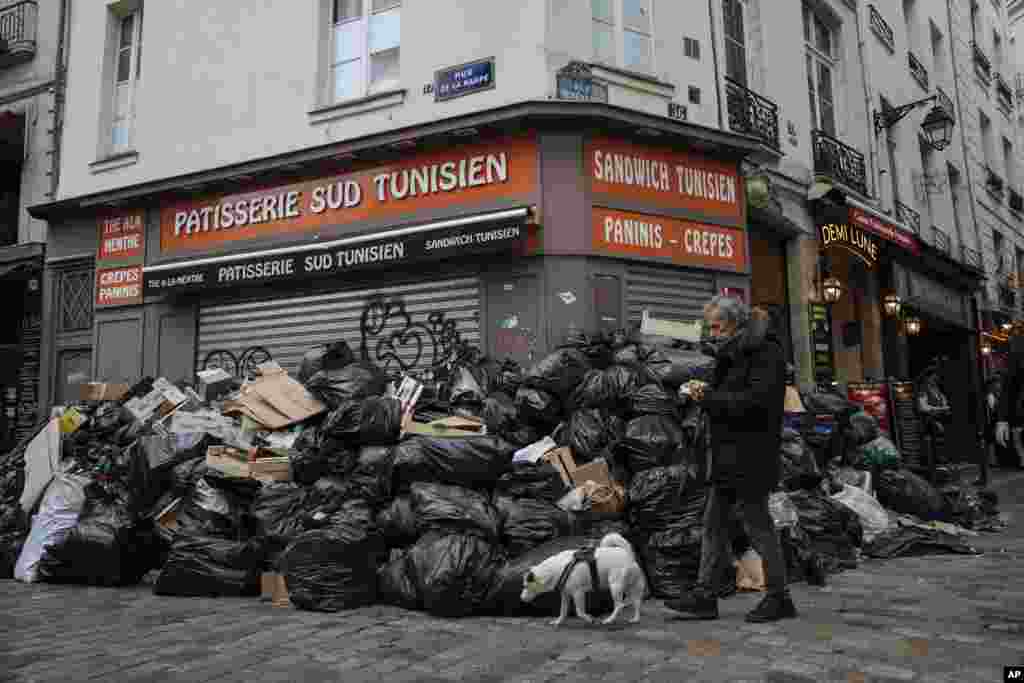 A man walks past piles of garbage in Paris, France. A contentious bill that would raise the retirement age in France from 62 to 64 got a push forward with the Senate's adoption of the measure amid strikes, protests and uncollected garbage piling higher by the day. 