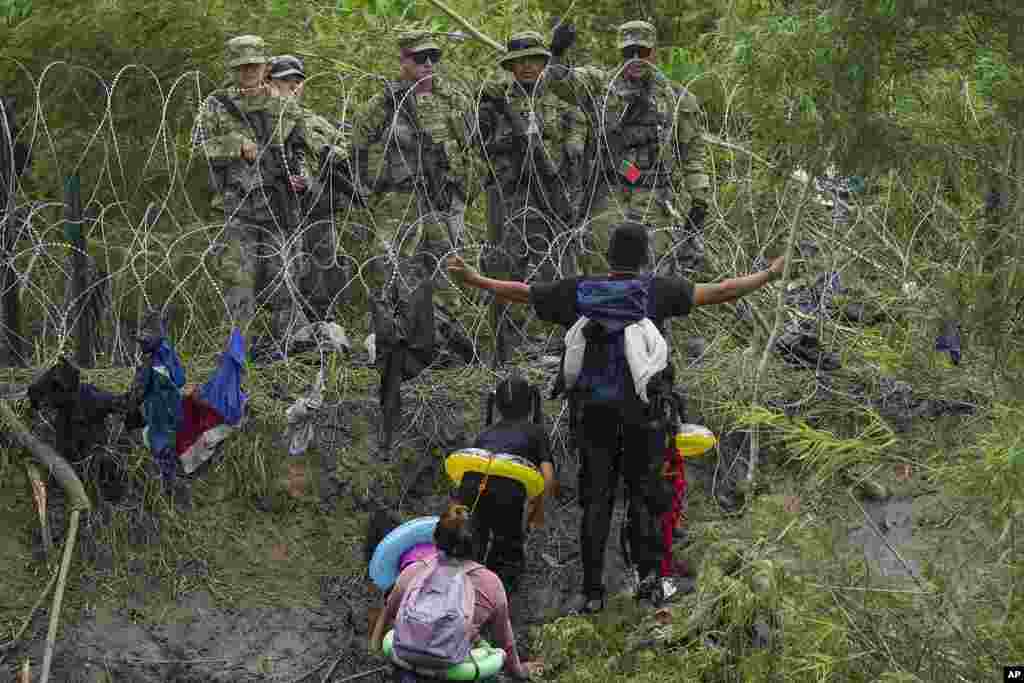 A migrant gestures to Texas National Guards standing behind razor wire on the bank of the Rio Grande River, seen from Matamoros, Mexico, as pandemic-related U.S. asylum restrictions, known as Title 42, expire.