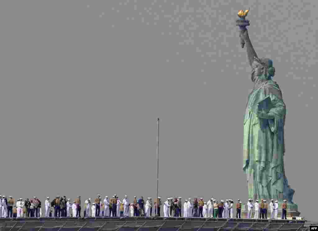 U.S. Sailors and Marines stand on the flight deck of the USS Bataan, a Wasp-class amphibious assault ship, as it passes the Statue of Liberty during Fleet Week in New York Harbor.