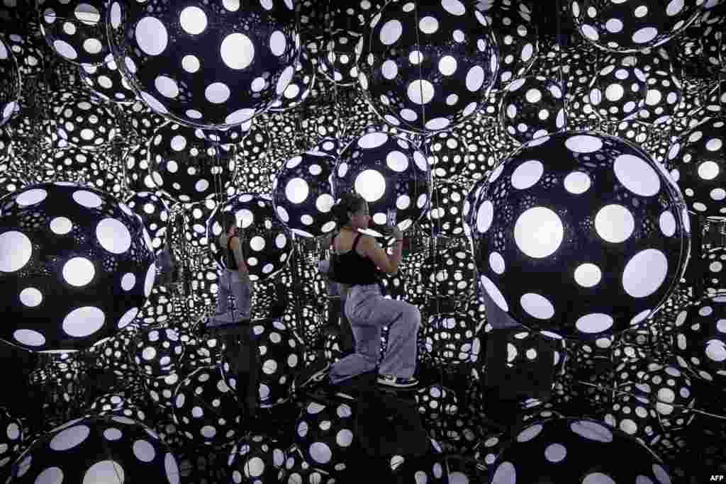 A woman takes photos at an art installation called Dots Obsession - Aspiring to Heavens Love by artist Yayoi Kusamas with her signature polka dots and reflective mirrors, in Hong Kong.