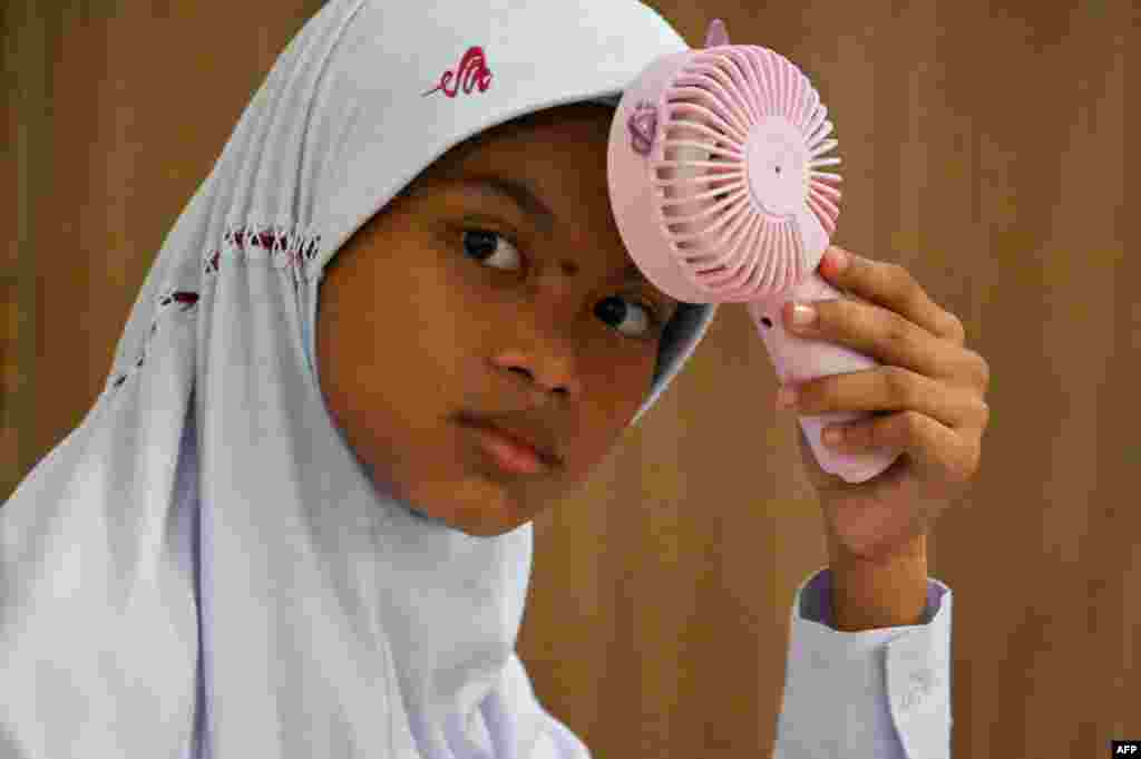 A primary school student uses a portable fan to keep cool in a classroom during hot weather in Banda Aceh, Indonesia.