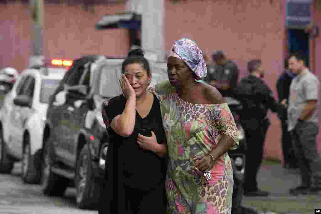 Silvia Palmieri, mother of a teacher who survived a stabbing attack at the Thomazia Montoro school, left, leaves the school comforted by a friend in Sao Paulo, Brazil. A 13-year-old student fatally stabbed a 71-year-old teacher and wounded three teachers and two fellow students in a knife attack at the public school, state officials said.