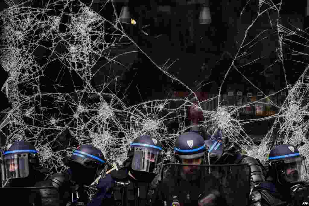 Police officers stand in front of the broken window of a shop during a demonstration on May Day (Labor Day) to mark the international day of the workers in Lyon, eastern France.