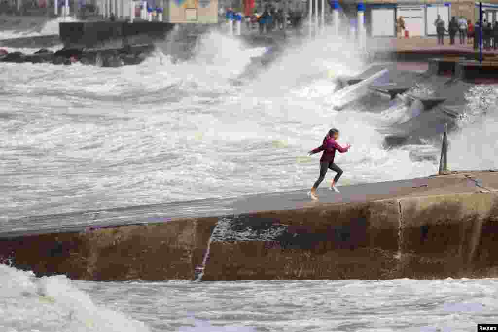 A girl runs on a dike while waves crash against a breakwater at high tide in Wimereux, as gusty summer winds hit northern and western France.