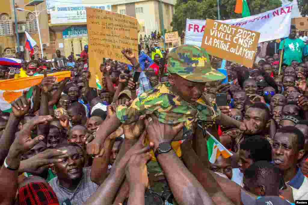 Men hold a child dressed in military uniform as they gather with thousands of anti-sanctions protesters in support of the putschist soldiers in the capital Niamey, Niger, Aug. 3, 2023.