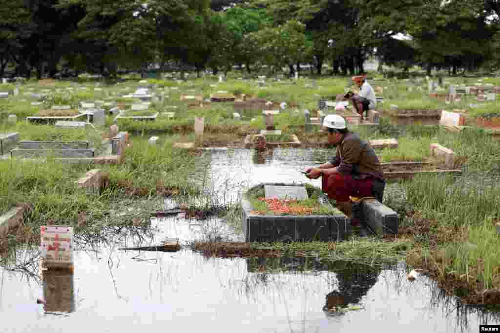 Men pray while visiting their relative's graves submerged in water due to heavy rain ahead of the holy fasting month of Ramadan, at the Semper cemetery complex in North Jakarta, Indonesia, March 8, 2024.
