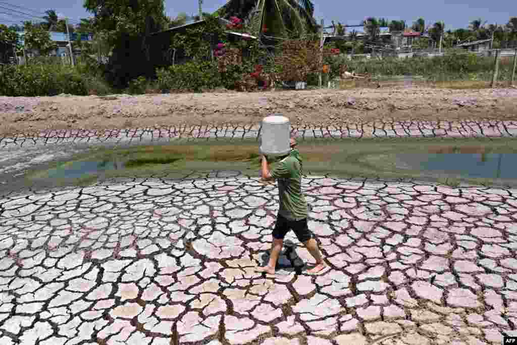 A man carries a plastic bucket across the cracked bed of a parched dried-up pond in Vietnam's southern Ben Tre province, March 19, 2024.