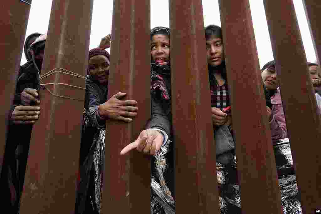 Migrants reach through a border wall for clothing handed out by volunteers, as they wait between two border walls to apply for asylum, in San Diego. Hundreds of migrants remain waiting between the two walls, many for days.