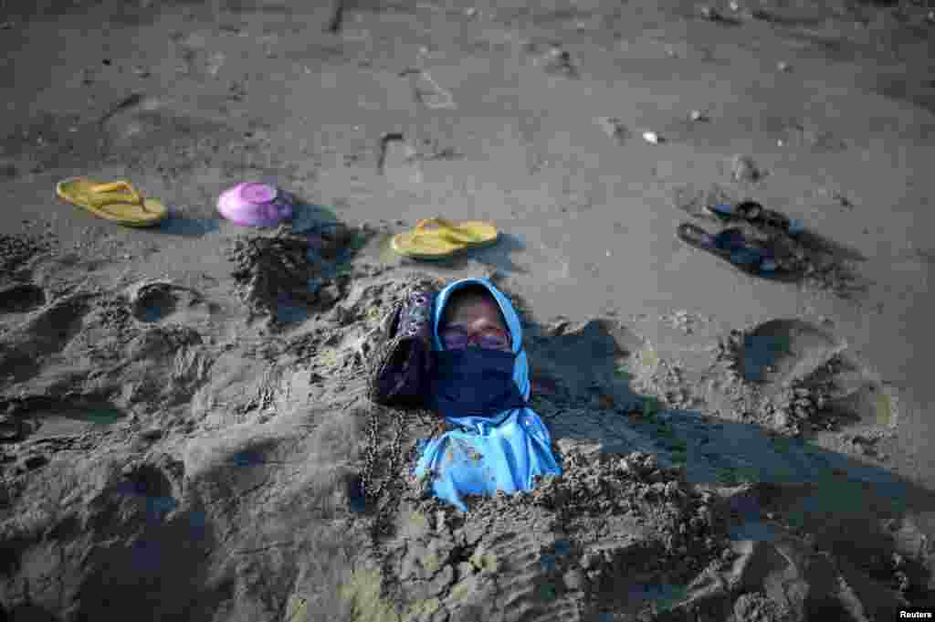 Nurmalawati lies covered with black sand during a traditional therapy, which is believed to have therapeutic properties, at Syiah Kuala beach in Aceh, Indonesia.
