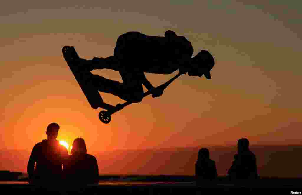 A young man performs a trick on a scooter during the sunset at a skate park on the sea wall of Calais, France, Aug. 15, 2023.