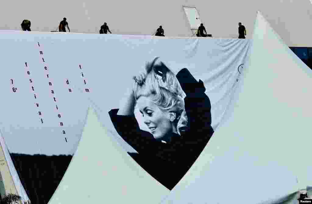 Workers set up a giant canvas of the official poster featuring Catherine Deneuve in the film La Chamade, on the facade of the festival palace ahead of the opening ceremony of the 76th Cannes Film Festival in Cannes, France, May 14, 2023.