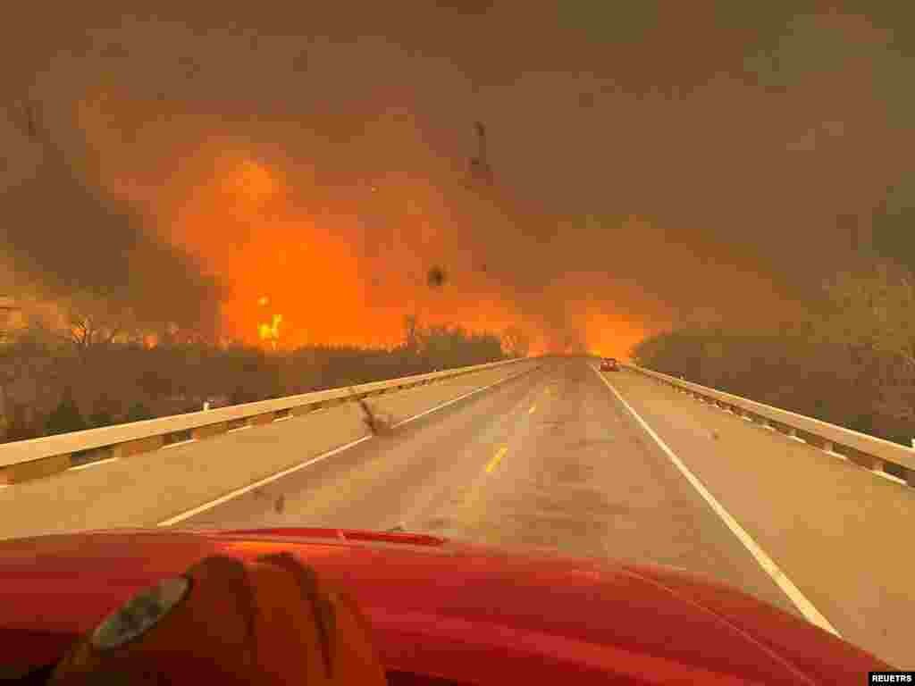Cars drive as smoke and fire rise from wildfires in a location given as Texas, U.S., in this handout picture released on Feb. 27, 2024. (Greenville Fire-Rescue/Handout)