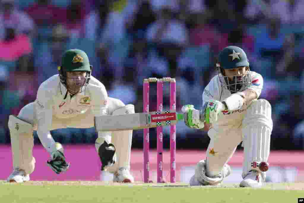 Pakistan's Mohammad Rizwan, right, sweeps the ball in front of Australia's Alex Carey on the third day of their cricket test match in Sydney.