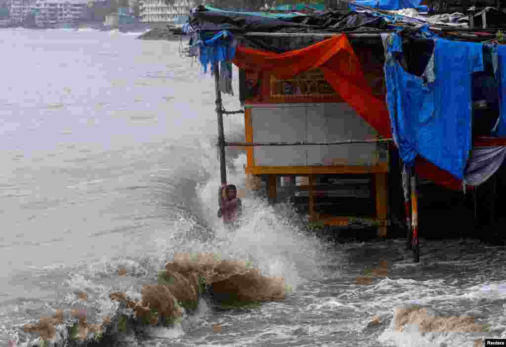 A man holds onto a bamboo pole to prevent himself from being swept away by waves during high tide at a beach in Mumbai, India.