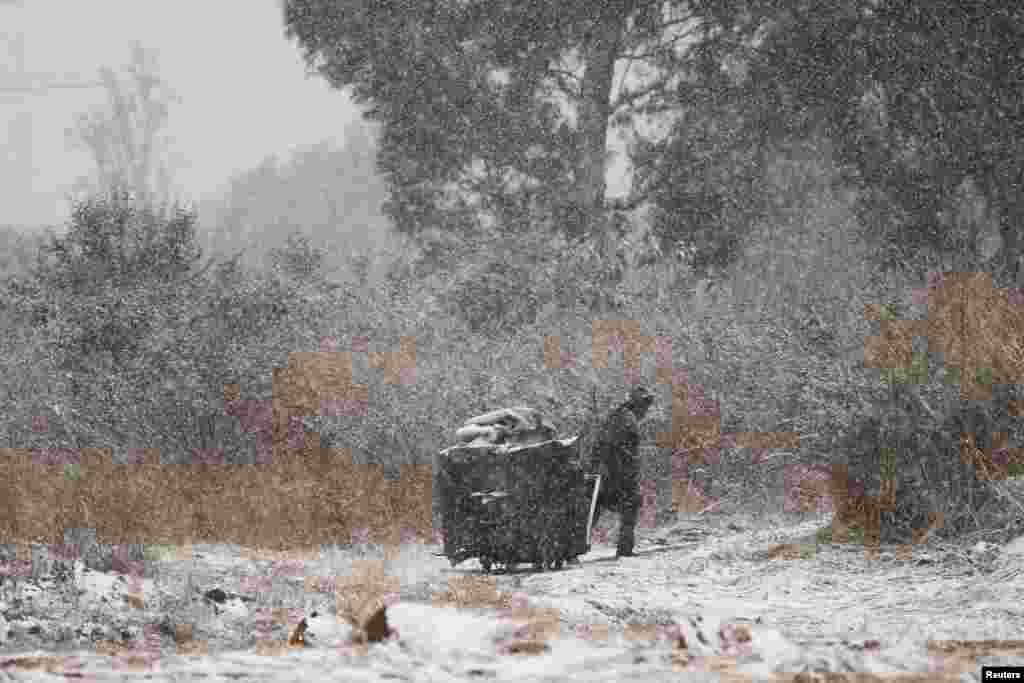 A garbage collector moves a trash bin amid snowfall in Brackenhurst, a suburb south of Johannesburg, South Africa.