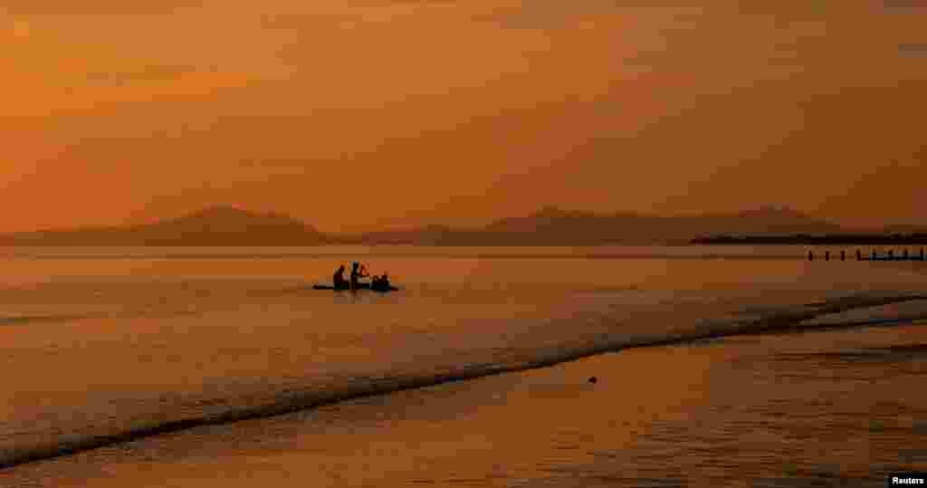 Children play on a paddleboard as the sun sets over the beach in Barmouth, Britain, May 29, 2023.